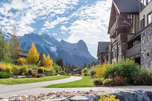 A mountain lodge with a paved walkway, autumn foliage, and a view of a mountain range. - Picturesque Views | Creekside Walking Paths to Town (Canmore)