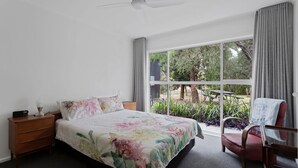 Una camera da letto con un'ampia finestra, un letto con biancheria da letto a motivi floreali, un comodino, una sedia e una ventola a soffitto.