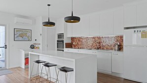 Una cucina moderna con mobili bianchi, una grande isola con sgabelli da bar, un forno a microonde e una parete di fondo rivestita di piastrelle.