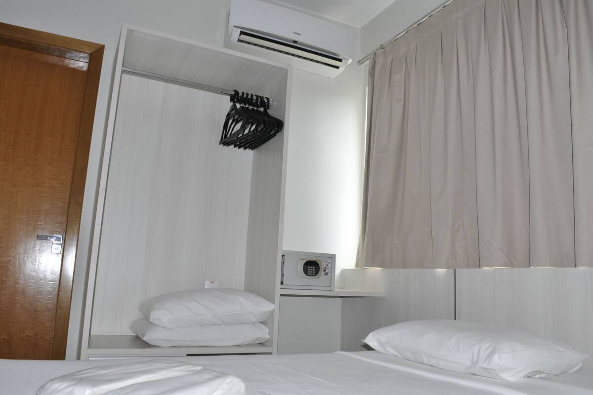 Quarto de hotel com uma cama, um guarda-roupa, um micro-ondas e uma cortina.