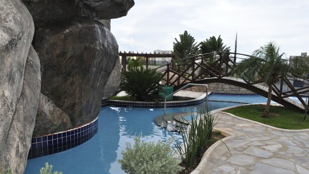 A swimming pool with a rock formation, a bridge, and a sign that reads "CINNA ADULTO". - Golden Dolphin Supreme - Achei Férias (Caldas Novas)