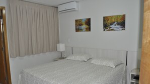 A neatly made bed with a patterned bedspread, a bedside table with a lamp, and two paintings on the wall. - Golden Dolphin Supreme - Achei Férias (Caldas Novas)