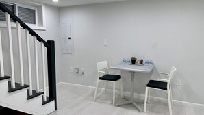Een kamer met een trap, een tafel met stoelen en een raam met jaloezieën.