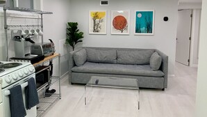 Een moderne keuken met een grijze bank, een transparante salontafel en drie ingelijste kunstwerken aan de muur.