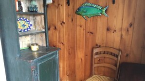 A wooden interior with a fish-shaped decoration, a wicker chair, and a shelf with decorative items. - Cozy Condo close to Sesuit (Dennis)