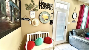 A living room with a white bench, a sofa, and decorative wall art including a welcome sign and a 'home sweet home' sign. - Ocean Breeze Vacation Townhouse (Gulfport)
