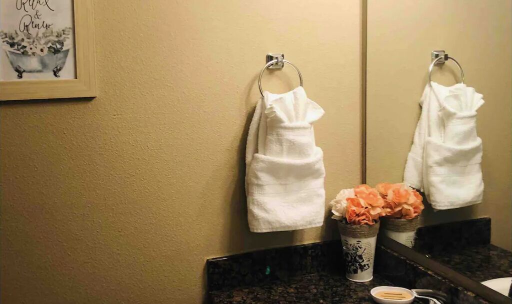 A bathroom with two white towels hanging on metal towel rings, a framed artwork on the wall, and a sink with a dark countertop.