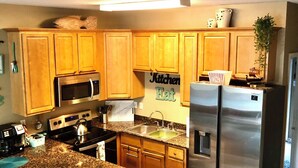 A modern kitchen with wooden cabinets, stainless steel appliances, and a central island with bar stools. - Ocean Breeze Vacation Townhouse (Gulfport)