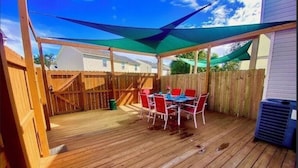 A wooden deck with a table and chairs, surrounded by a wooden fence and a green canopy. - Ocean Breeze Vacation Townhouse (Gulfport)