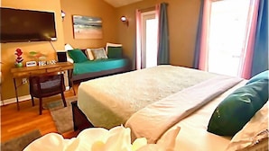 A hotel room with a bed, a desk, a chair, a ceiling fan, and a window with curtains. - Ocean Breeze Vacation Townhouse (Gulfport)