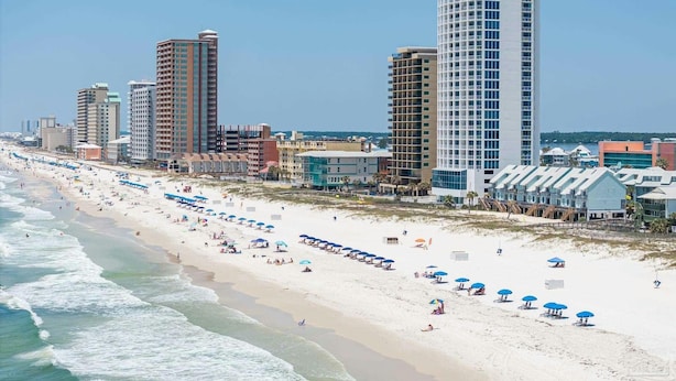A beach with rows of umbrellas and a row of high-rise buildings in the background.