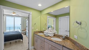 A bedroom with a bed, a balcony with a view, and a bathroom with two sinks and a large mirror.