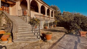 Ein Gebäude mit einer Treppe, die zu einem überdachten Bereich mit Bögen führt, umgeben von Blumentöpfen und blauem Himmel.