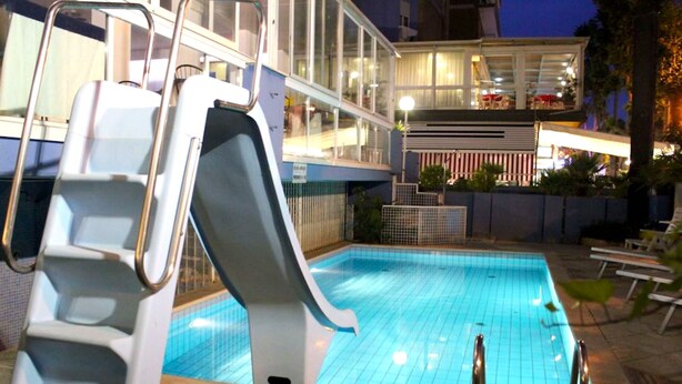 Ein Pool mit Rutsche, umgeben von Liegestühlen und einem Gebäude mit Balkon.