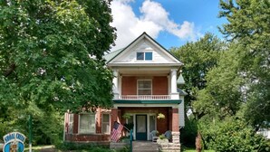 A two-story house with a front porch, a brick facade, and a number '101' on the front door. - The Estate Room at Shoal Creek B&B (Hamilton)