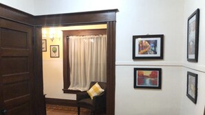 A room with a wooden door, a patterned rug, a chair with a cushion, and framed pictures on the wall. - The Estate Room at Shoal Creek B&B (Hamilton)