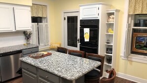 A kitchen with a granite countertop, white cabinets, a stainless steel dishwasher, a black refrigerator, and a dining area with a table and chairs. - The Estate Room at Shoal Creek B&B (Hamilton)