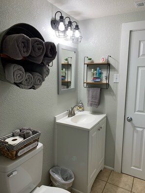 A bathroom with a white sink, a mirror, and a towel rack. There are towels and toiletries on shelves.