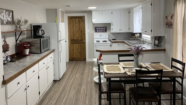A modern kitchen with white cabinets, a wooden door, and a dining area with a table and chairs. - Private Country Farmhouse (Winnsboro)