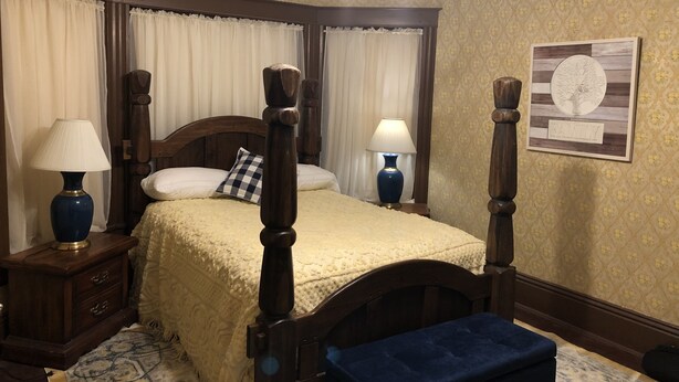 A neatly arranged bedroom with a four-poster bed, two bedside tables with lamps, a decorative wall piece, and a patterned rug. - The Cottage Room at Shoal Creek B&B (Hamilton)