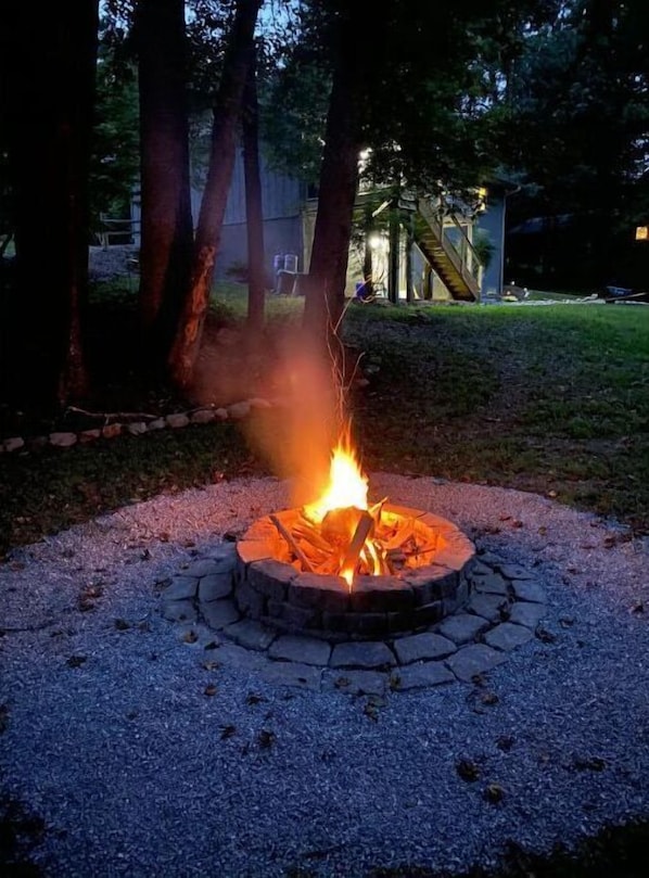 A circular stone fire pit with a fire burning in the center, surrounded by a gravel area.