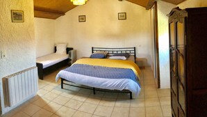 A bedroom with a bed, a bedside table, a radiator, and a wooden wardrobe. - Cottage near Barjac (Saint-Privat-de-Champclos)