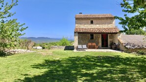 A stone house with a tiled roof, a small porch with chairs, and a view of the countryside. - Cottage near Barjac (Saint-Privat-de-Champclos)