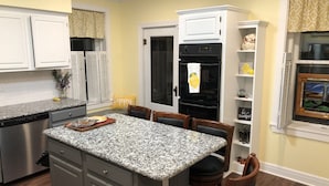 A kitchen with a granite countertop, white cabinets, a stainless steel dishwasher, a black refrigerator, and a dining area with a table and chairs.