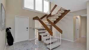 A spacious hallway with a polished tile floor, a wooden staircase with white railings, and a door with a key in the lock. - Feels Like Home - w/ Heated Pool Book Now! (Punta Gorda)