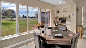 A dining area with a large table, chairs, and a view of a grassy field through large windows. - Feels Like Home - w/ Heated Pool Book Now! (Punta Gorda)