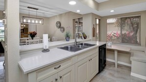 A modern kitchen with a white countertop, stainless steel sink, and a dishwasher. There are decorative plates on the wall and a potted plant on the counter. - Feels Like Home - w/ Heated Pool Book Now! (Punta Gorda)