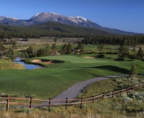 Un campo de golf con una valla de madera, un estanque y montañas al fondo.