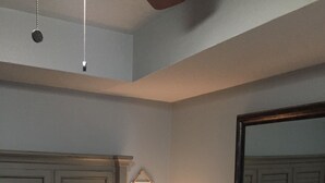 Un dormitorio con cama, almohadas, mesita de noche con lámpara y espejo en la pared.