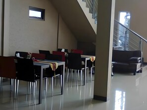 A dining area with tables and chairs, a staircase, and a view of the outside.
