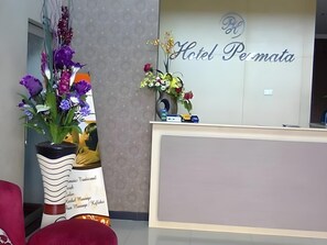 A hotel reception desk with a sign that reads 'Hotel Permata.' There are two vases with flowers in front of the desk.