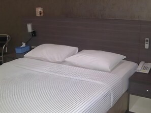 A hotel room with a neatly made bed, a bedside table with a lamp, and a telephone.