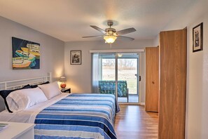 A bedroom with a bed, a ceiling fan, a window, and a door leading to a balcony.