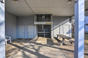 A covered outdoor area with a 'WELCOME' sign, a bench, and a staircase leading to a building with closed doors.