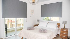 A bedroom with a large bed, a nightstand, a lamp, and a view of the outside. - Villa Alba, Luxury 4 BDRM Villa with Heated Pool (Protaras)