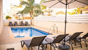 A rooftop pool area with a rectangular pool, black lounge chairs, and a large umbrella providing shade. - Villa Alba, Luxury 4 BDRM Villa with Heated Pool (Protaras)