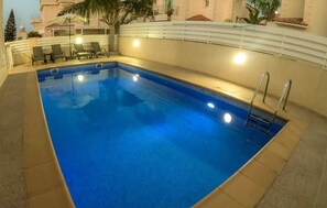A rectangular swimming pool with a clear blue water surface, surrounded by a tiled deck. There are lounge chairs and a small table near the pool's edge. - Villa Alba, Luxury 4 BDRM Villa with Heated Pool (Protaras)