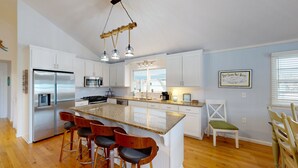 Una cocina moderna con armarios blancos, electrodomésticos de acero inoxidable, encimera de granito y una zona de bar con taburetes.