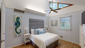 Un dormitorio con una cama grande, un ventilador de techo, una ventana con persianas y un cuadro en la pared.