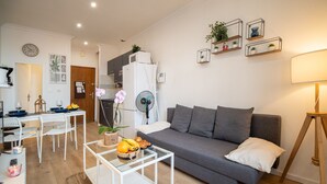 A modern living room with a grey sofa, a glass coffee table, a dining area with a white table and chairs, and a kitchen area with a fridge and microwave. - Lovely & Independant - Queen size bed, netflix, wifi (Lourdes)