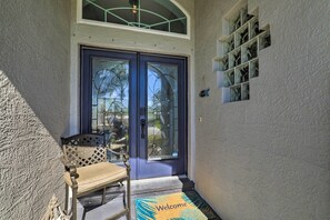 Entrada de casa com porta azul, um banco e tapete de boas-vindas.