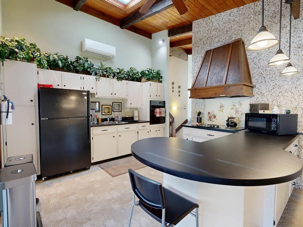 Cozinha moderna com ilha central, armários brancos e geladeira preta.