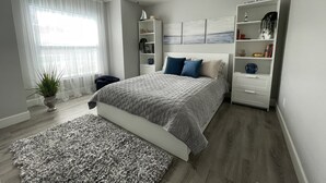 A bedroom with a bed, a ceiling fan, a window with sheer curtains, a bedside table, a nightstand, a bookshelf, and a potted plant. - Water Front Boundary Vacation Home Villa close to beaches, golfing, Fishing (Rotonda West)