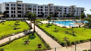Ein modernes Hotel mit Schwimmbad, umgeben von gepflegten Rasenflächen und Palmen.