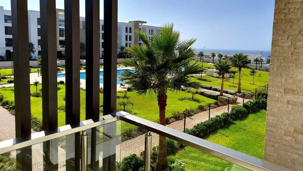 Ein Balkon mit Blick auf einen Swimmingpool, Palmen und moderne Gebäude.