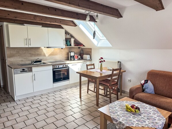 Cocina compacta con muebles blancos, horno integrado y comedor con mesa y sillas.
